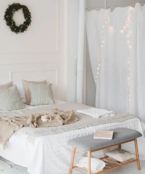 Bed met beige gebreide ruitjes en een kopje. Interieur van stijlvolle gezellige slaapkamer met krans aan de muur. Kerstmis, Nieuwjaar home decor — Stockfoto