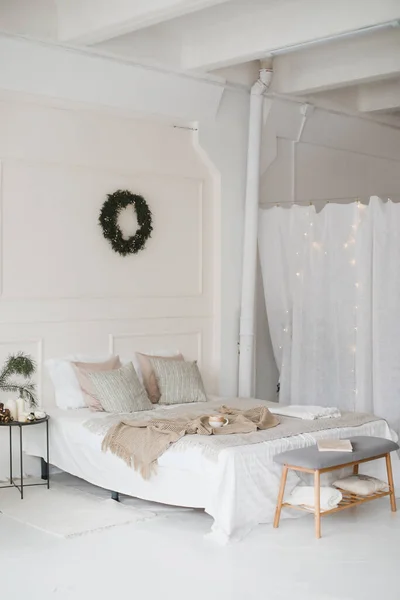 Bed met beige gebreide ruitjes en een kopje. Interieur van stijlvolle gezellige slaapkamer met krans aan de muur. Kerstmis, Nieuwjaar home decor — Stockfoto