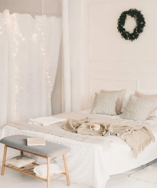 Bed met beige gebreide ruitjes en een kopje. Interieur van stijlvolle gezellige slaapkamer met krans aan de muur. Kerstmis, Nieuwjaar home decor — Stockfoto