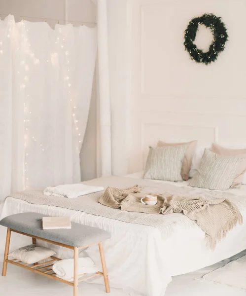 Cama com xadrez de malha bege e uma xícara. Interior de elegante quarto acolhedor com grinalda na parede. Natal, decoração da casa do ano novo — Fotografia de Stock