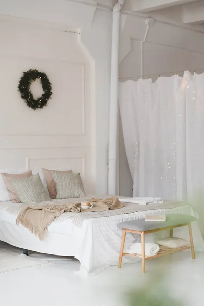 Bed met beige gebreide ruitjes en een kopje. Interieur van stijlvolle gezellige slaapkamer met krans aan de muur. Kerstmis, Nieuwjaar home decor — Stockfoto