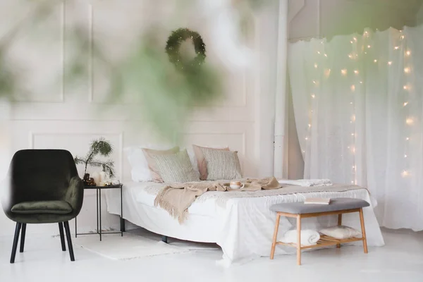 Bed met beige gebreide ruitjes en een kopje. Interieur van stijlvolle gezellige slaapkamer met krans aan de muur. Kerstmis, Nieuwjaar home decor — Stockfoto