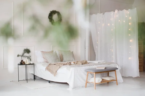 Łóżko z beżową, dzianinową kratą i filiżanką. Wnętrze stylowej przytulnej sypialni z wieńcem na ścianie. Boże Narodzenie, Nowy Rok dekoracji domu — Zdjęcie stockowe