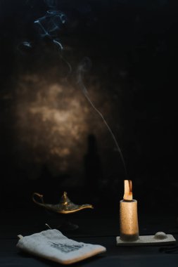 Palo Santo şamdandaki dumanla devam ediyor. Meditasyon, rahatlama konsepti. Palo santo ağacı, koyu arkaplanda akromatik çubuklar.