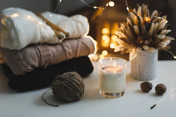 Knitted woolen sweaters, needles, candles against bokeh lights background. Hygge cozy mood still life. Winter, New Year background — Stock Photo, Image