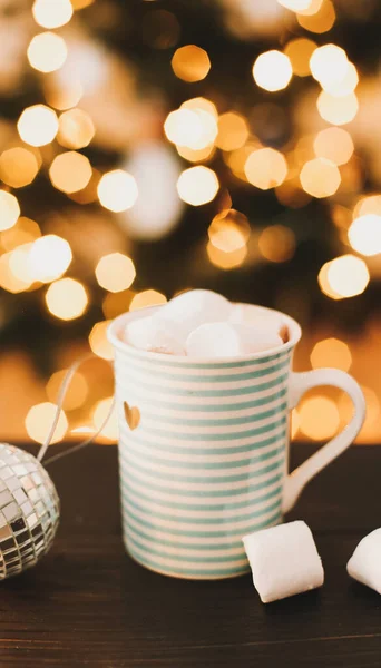 Tazza di caffè con marshmallow con albero di Natale sfocato sullo sfondo, ornamento natalizio. Natale e Capodanno atmosfera accogliente — Foto Stock