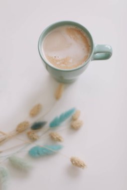 Beyaz arka planda bir fincan kahve ve kurutulmuş çiçekler. Sıcak köpüklü kapuçino kaplı yeşil kupa.