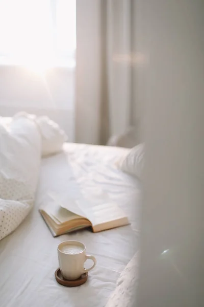 Tasse à café avec mousse de lait et un livre sur un drap de lit blanc. — Photo