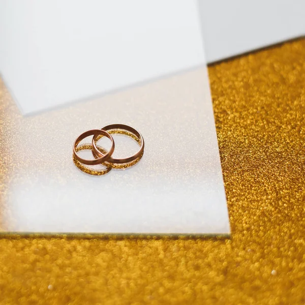 Két arany jegygyűrű arany háttérrel. — Stock Fotó