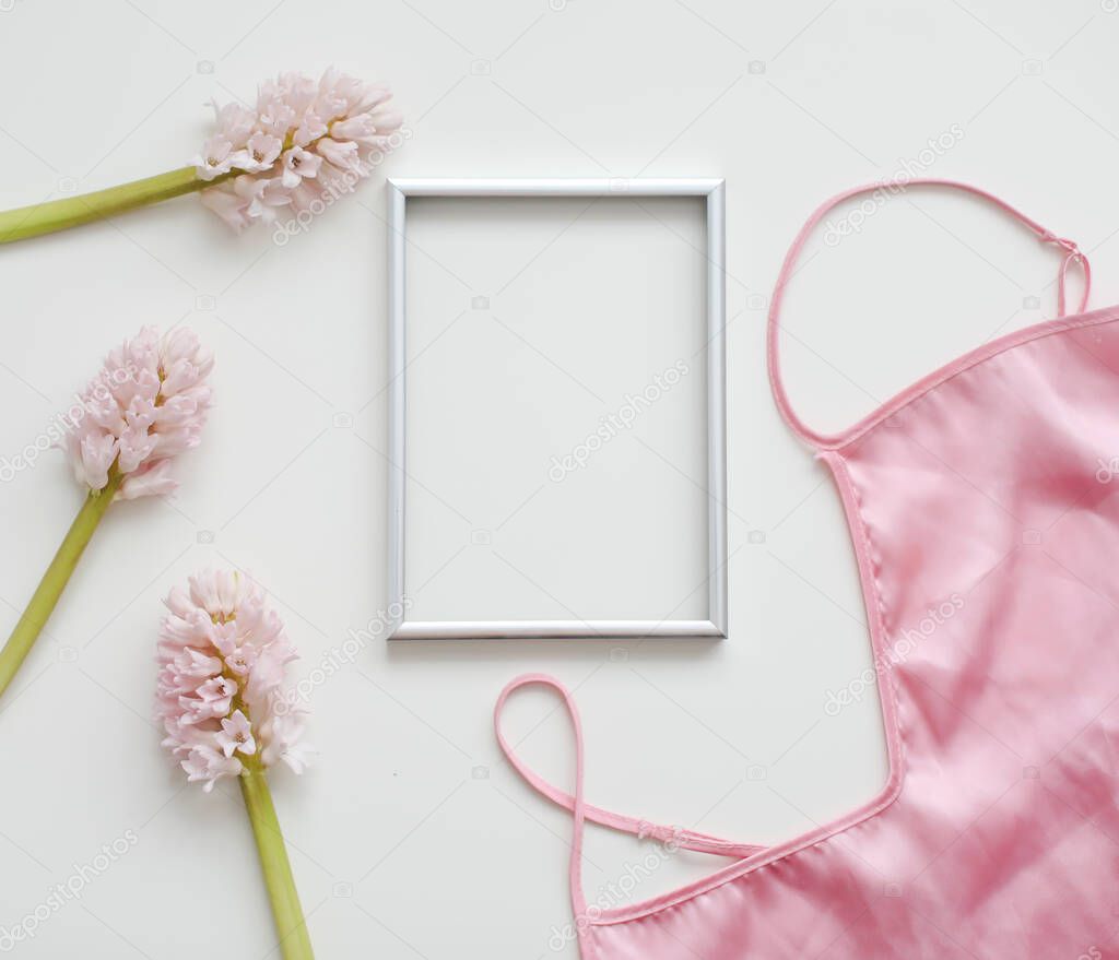 Styled feminine flat lay with blank photo frame, silk lingerie and pink flowers on white background. top view, copy space. 