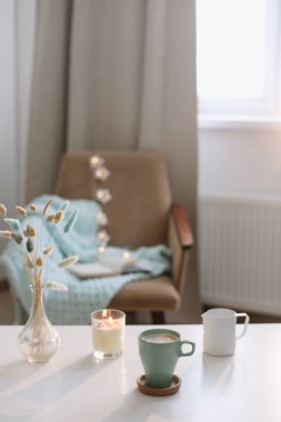Bir fincan kahve, mum ve kahve masasında çiçekler olan bir vazo ile yaşam tarzı kompozisyonu. Konforlu ev dekorasyonu konsepti