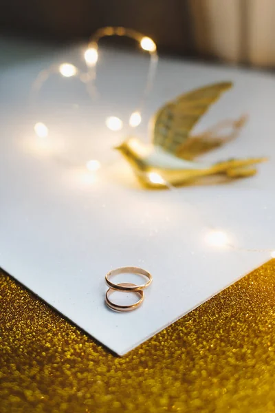 금빛 결혼반지에 장난감 새 와장 식물이 그려져 있다. 반짝 이는 황금 장신구. 결혼식 세부 사항. 결혼의 제안, 발렌타인데이 선물. 복사 공간. — 스톡 사진