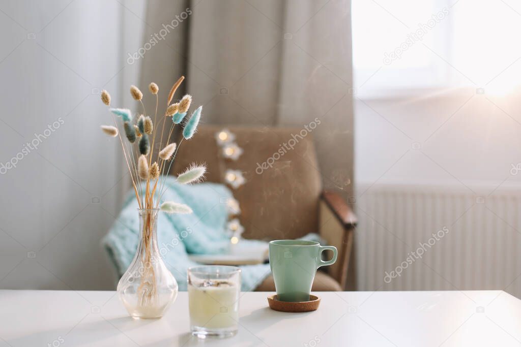 Lifestyle composition with cup of coffee, candle and a vase with flowers on a coffee table. Cozy home interior decoration concept