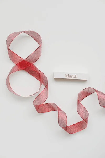 Červená stuha a slovo MARCH na bílém pozadí. 8. března, koncept Mezinárodního dne žen. — Stock fotografie