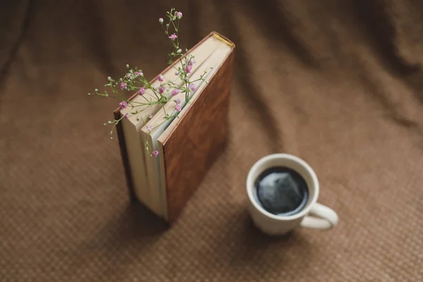 Un livre avec des fleurs et une tasse de café sur fond sombre vue de dessus — Photo