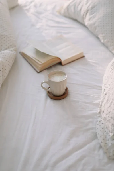 Livro aberto sobre lençóis e uma xícara de café. Bom dia. Pequeno-almoço na cama. deitado plano — Fotografia de Stock