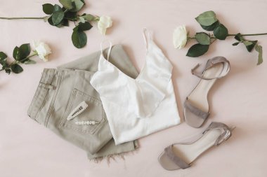 Bej arka planda kot pantolon, sandalet ve çiçek demeti. Kadın günlük bahar kıyafetlerinin en üst görüntüsü. Moda tarzı kadın kıyafetleri. Düz yatıyordu