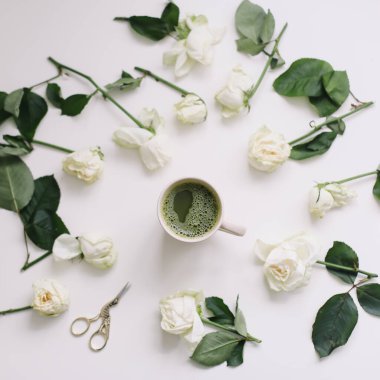 Beyaz arka plan manzaralı beyaz güllü bir fincan yeşil çay. Düz görünüm, üst görünüm, boşluk kopyala. 