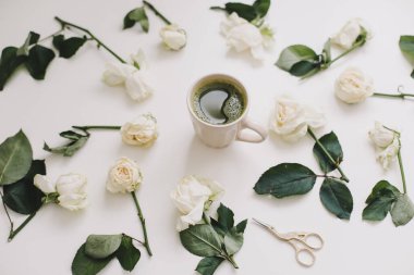 Beyaz arka plan manzaralı beyaz güllü bir fincan yeşil çay. Düz görünüm, üst görünüm, boşluk kopyala. 