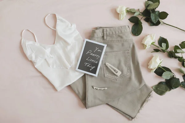 Bovenaanzicht van vrouwen casual lente zomer outfit. Jeans, sandalen, accessoires en bloemen op beige achtergrond. Vlakke lay, bovenaanzicht. — Stockfoto