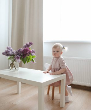 cute little girl in a pink dress with a bouquet of fragrant lilacs at home