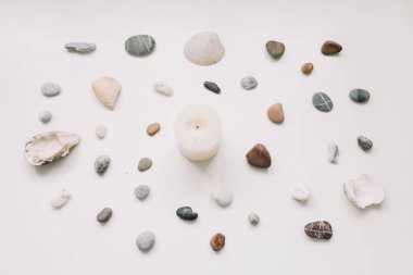 Spa background with sea shells and pebbles and white candle on white. Flat lay, top view, minimal spa concept