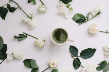 A cup of matcha tea and roses on white background. Flatlay, top view