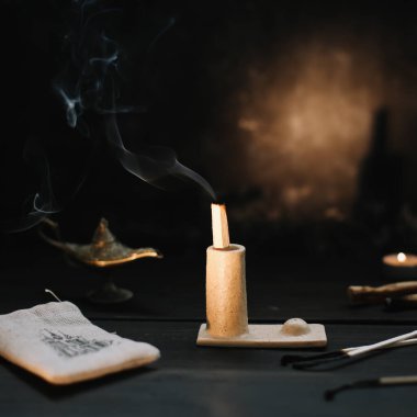 Palo Santo güzel bir şamdanda dumanla yanıyor. İyileşme, meditasyon, rahatlama, arındırma konsepti. Palo santo ağacı, koyu arkaplanda akromatik çubuklar. Evde sıcak bir akşam..
