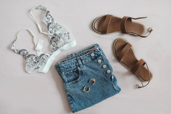 Platte lay compositie met vrouwelijke lingerie, denim shorts en sandalen op beige achtergrond bovenaanzicht — Stockfoto