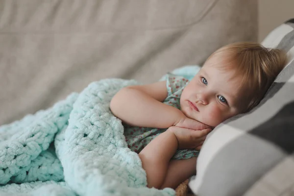 Linda niña de dos años yaciendo bajo cuadros en casa — Foto de Stock