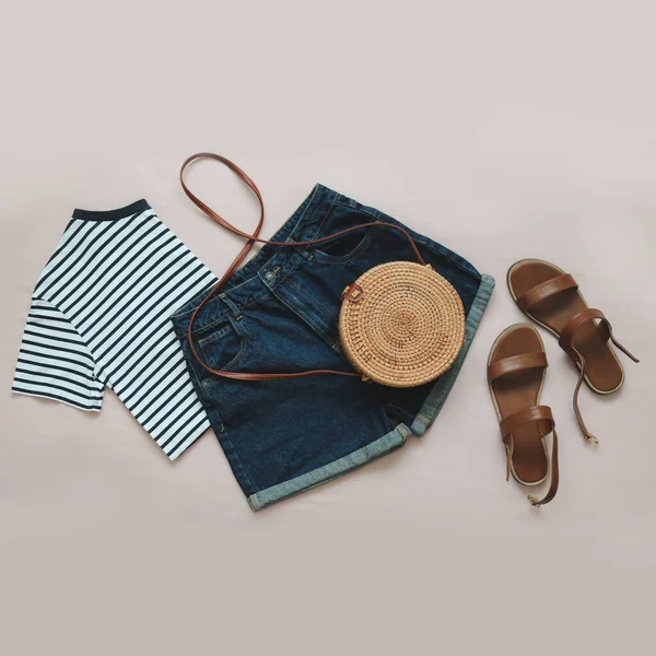 Плоска композиція з жіночим верхом, джинсові шорти, сандалі та плетений мішок з ротанга на бежевому тлі вид зверху — стокове фото