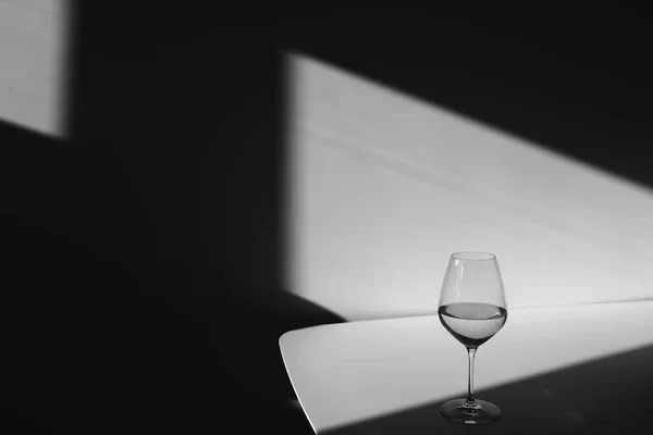 Szklanka wody na białym tle z cieniem. Chiaroscuro z okna. Czarno-białe zdjęcie. Zbliżenie, przestrzeń kopiowania — Zdjęcie stockowe