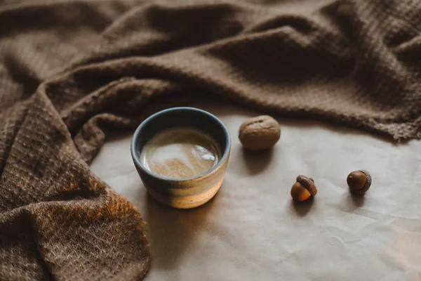 Cup of cappuccino on a brown paper texture background with cozy warm plaid, walnuts and acorns