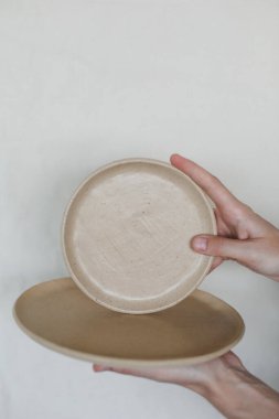 Beyaz arka planda izole edilmiş seramik tabakları tutan eller. El yapımı seramik sofra takımı ve çömlek takımı.