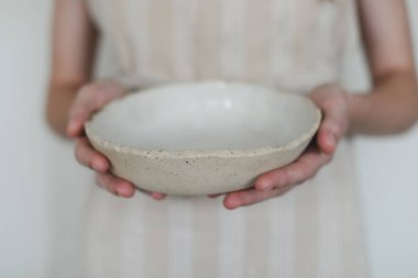 Beyaz arka planda izole edilmiş seramik kaseyi tutan eller. El yapımı seramik sofra takımı ve çömlek