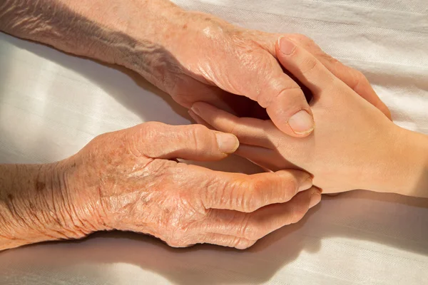 Händerna på mormor och barnbarn i sängen — Stockfoto