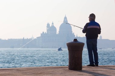VENICE, İtalya - 14 Mart 2014: Riva S. Biagio rıhtımından balıkçı ve Santa Maria della Salute Kilisesi 'nin silueti.