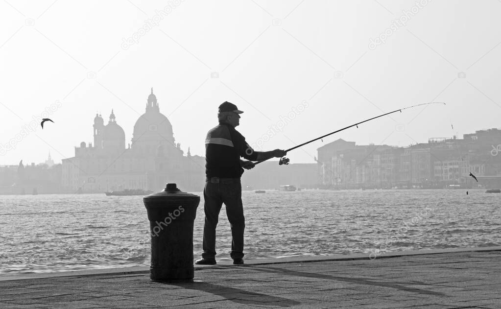 VENICE, ITALY - MARCH 14, 2014: Fisherman from Riva S. Biagio waterfront and silhouette of Santa Maria della Salute church.