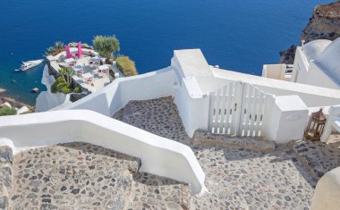 Santorini - Restoran, Oia 'da romantik bir restorana (Ia) ve arka plandaki kayalıkların altındaki yata hazırlanıyor..
