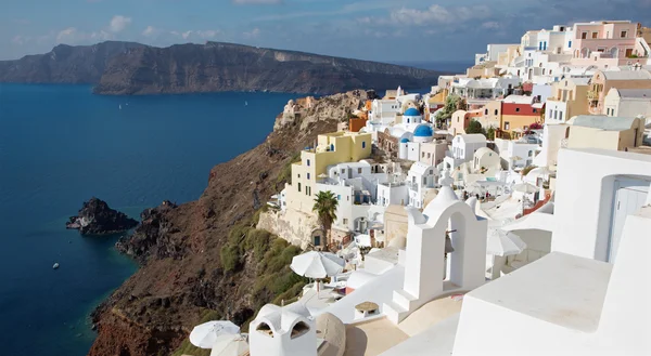 Santorini - La mirada a las cúpulas de la iglesia típicamente azul en Oia sobre la caldera y la isla Therasia en el fondo. —  Fotos de Stock