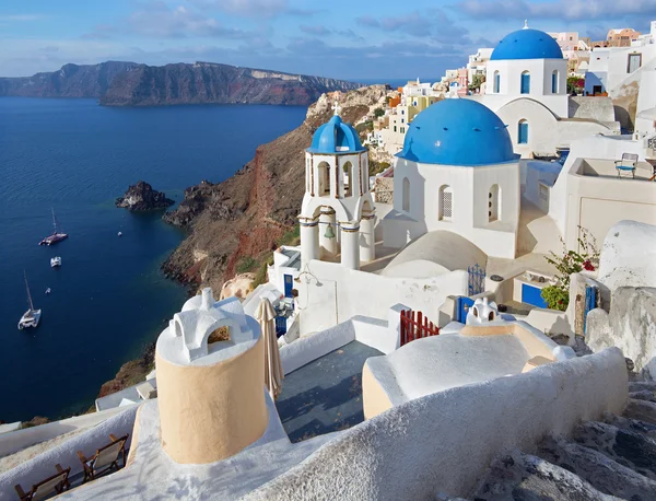 Santorini - De blik op typisch blauwe kerk koepels in Oia over de caldera en het eiland Therasia op de achtergrond. Stockfoto