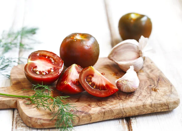 Whole, cut tomatoes and garlic in cutting board — Stock Photo, Image