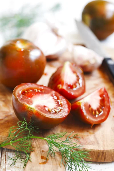 Whole, cut tomatoes and garlic in cutting board — Stock Photo, Image