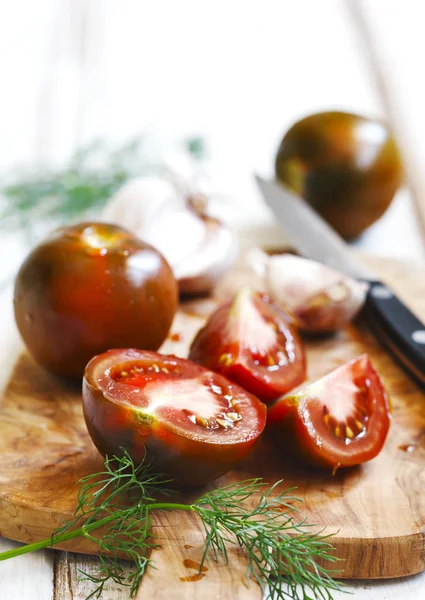 Whole, cut tomatoes and garlic in cutting board — Stock Photo, Image