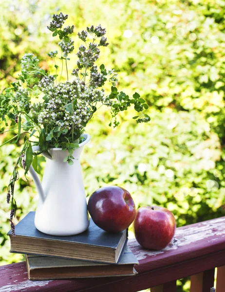 Fiori selvatici estivi in vaso di vetro, vecchi libri e mele . — Foto Stock