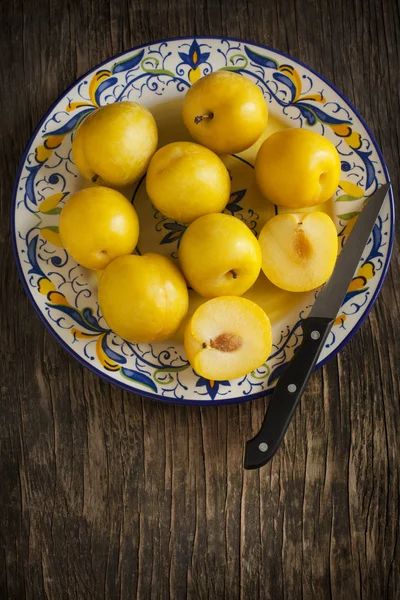 Čerstvé žluté švestky v talíř na dřevěné pozadí — Stock fotografie