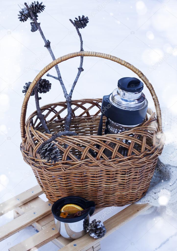 Basket with thermos of mulled wine and knitted blanket on sledge