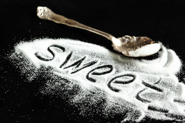 Wort "süß" in Zucker auf schwarzem Hintergrund geschrieben. — Stockfoto