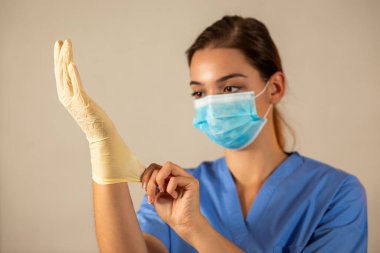 Mavi cerrahi maskeli genç hemşire koruyucu lastik eldiven giyiyor..