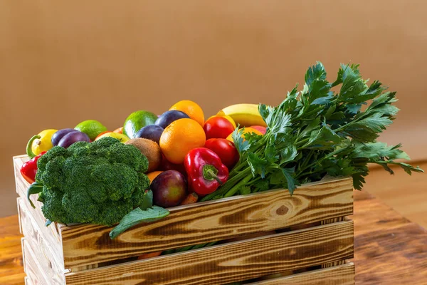 Деревянная коробка свежих фруктов и овощей на коричневом столе. — стоковое фото